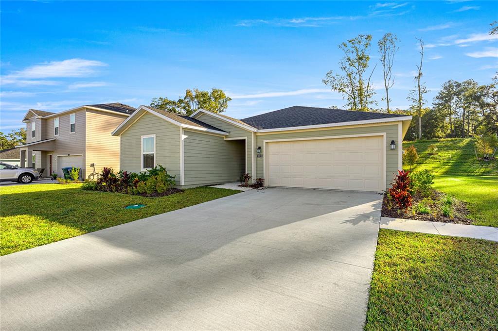 A single-story house with light green siding and a two-car garage under a blue sky — 16983 NW 144TH STREET, ALACHUA, FL