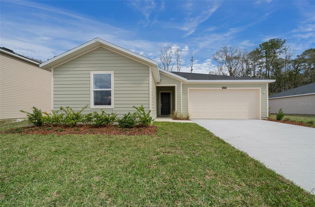 A single-story house with light green siding, a two-car garage, and a front lawn — 16983 NW 144TH STREET, ALACHUA, FL