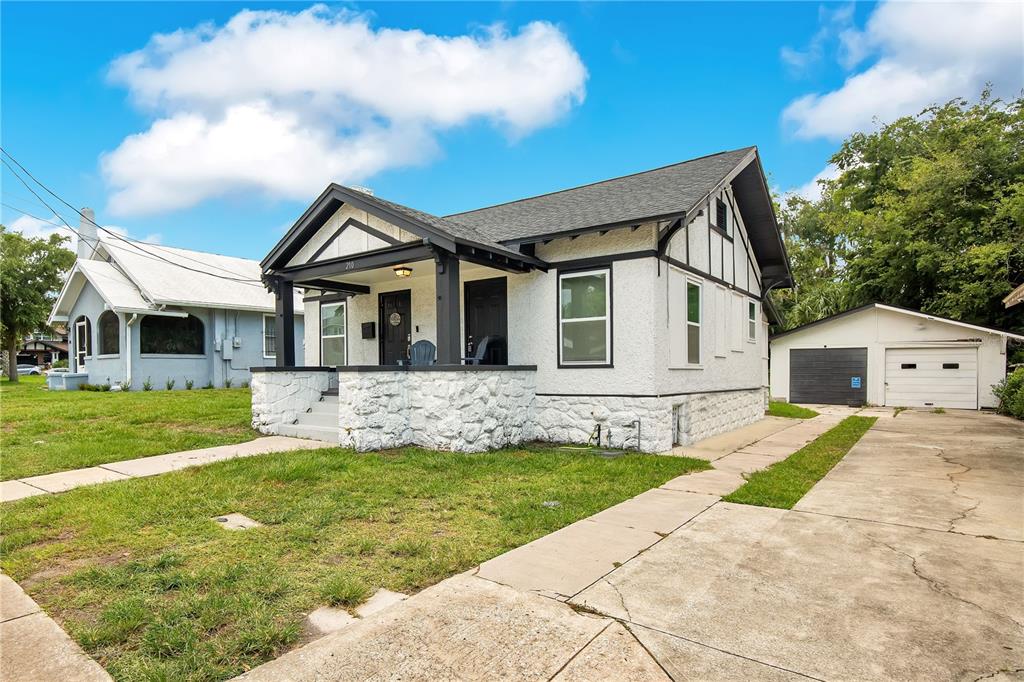 A white stucco bungalow with a stone porch and detached garage under a blue sky — 210 BELLEVUE AVENUE, DAYTONA BEACH, FL