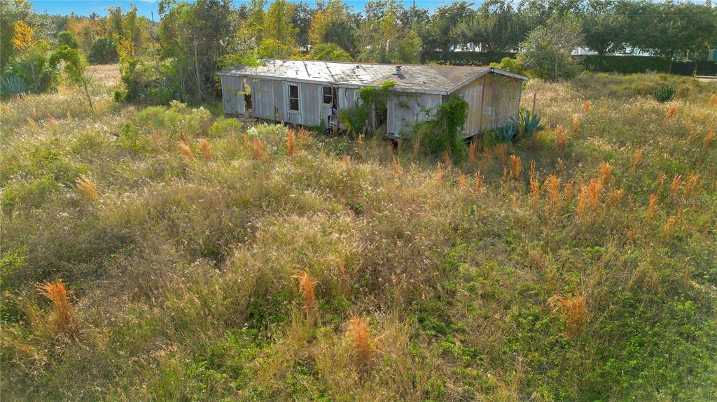 An aerial view shows a dilapidated, weathered mobile home situated in an overgrown, grassy field — 28432 S EICHELBERGER ROAD, TAVARES, FL
