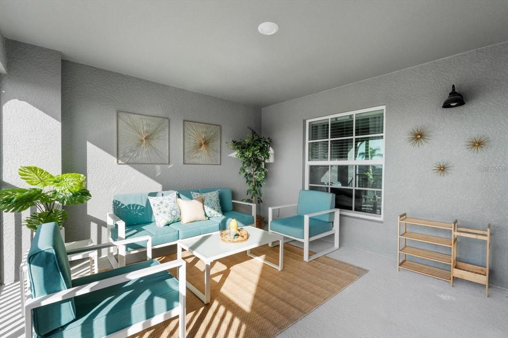 A covered patio features a blue sofa, matching chairs, a coffee table, and wall decor — 12440 WELLEN GOLF STREET UNIT 203, VENICE, FL