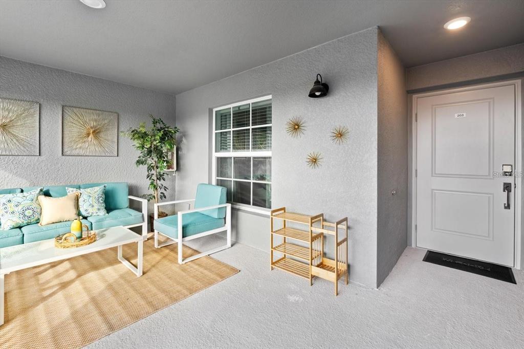 A furnished outdoor patio features a sofa, armchair, shoe rack, and a white entry door — 12440 WELLEN GOLF STREET UNIT 203, VENICE, FL