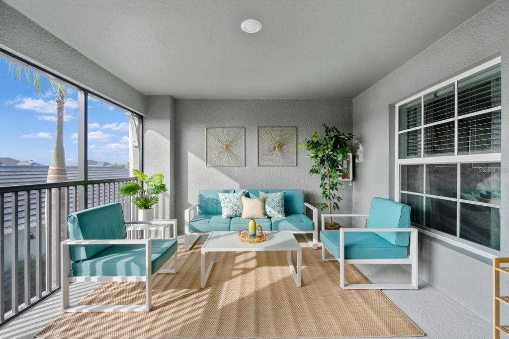A covered patio features white metal furniture with teal cushions on a tan area rug — 12440 WELLEN GOLF STREET UNIT 203, VENICE, FL