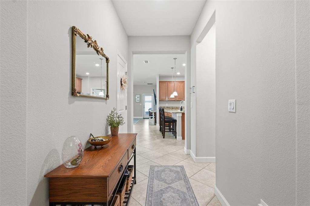 A hallway with a wooden console table and mirror leads to an open kitchen area — 11804 VALHALLA WOODS DRIVE, RIVERVIEW, FL