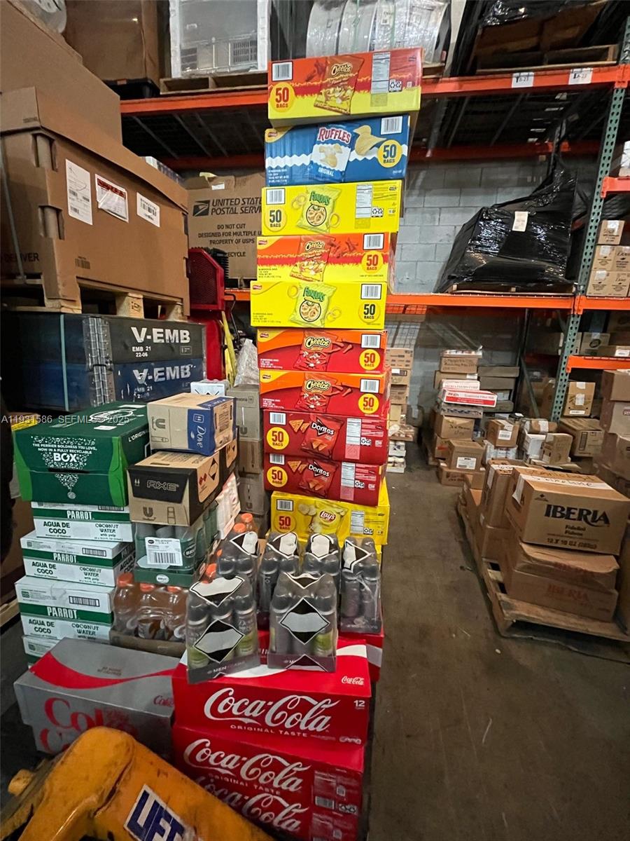 A warehouse storage area features tall stacks of snack boxes, beverage cases, and cardboard shipping containers — 79th, Miami FL 33166, MIAMI, FL