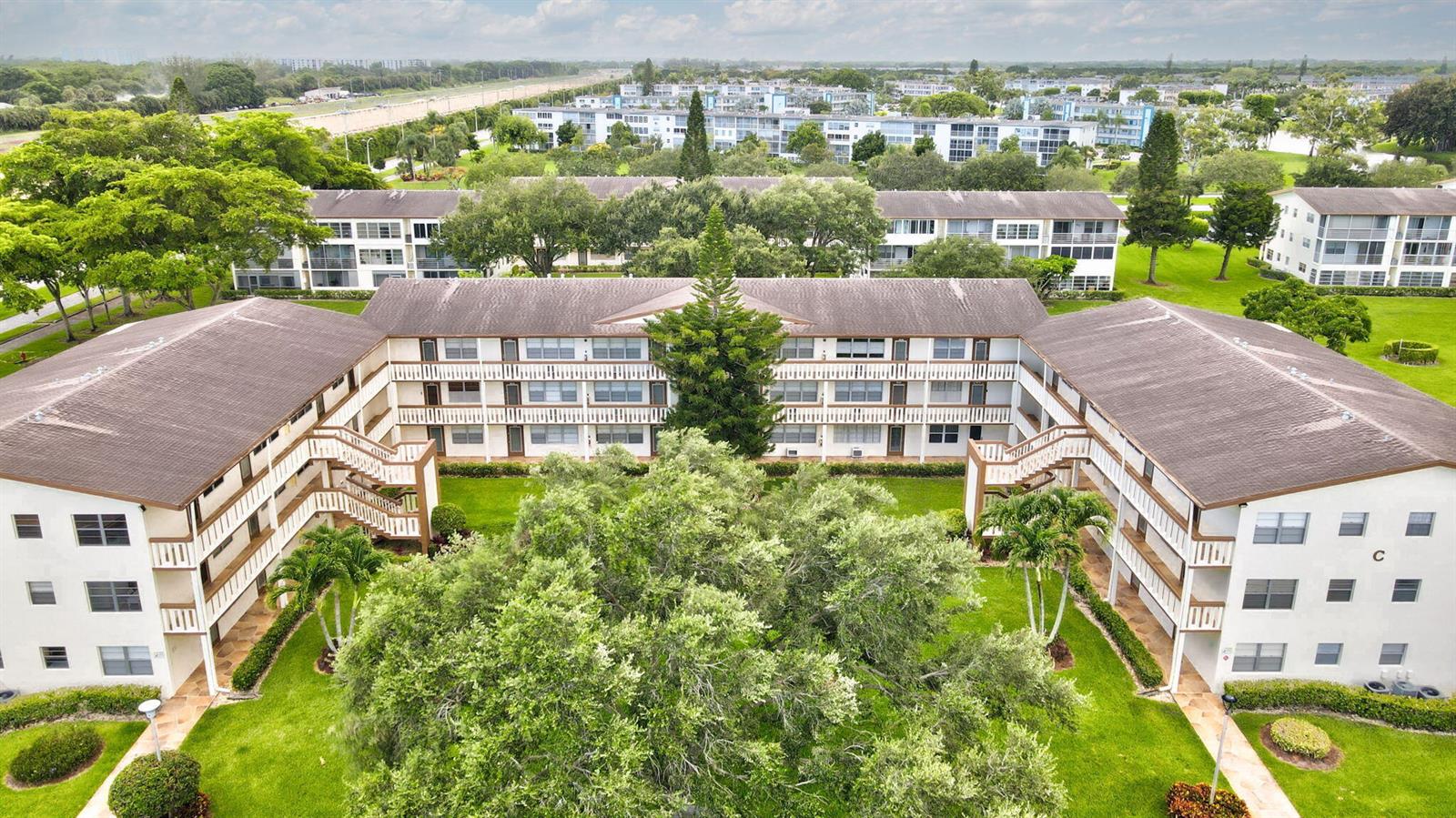 An aerial view shows a U-shaped apartment complex surrounding a grassy courtyard with trees — 104 Mansfield C Drive # C, Boca Raton FL 33434, BOCA RATON, FL