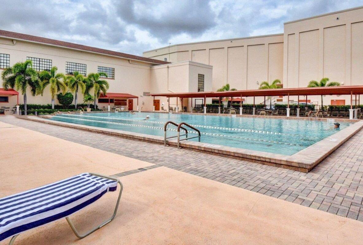 An outdoor swimming pool with a striped lounge chair on a paved deck — 104 Mansfield C Drive # C, Boca Raton FL 33434, BOCA RATON, FL