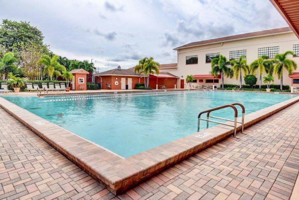 A large outdoor swimming pool is surrounded by a brick patio and palm trees — 104 Mansfield C Drive # C, Boca Raton FL 33434, BOCA RATON, FL
