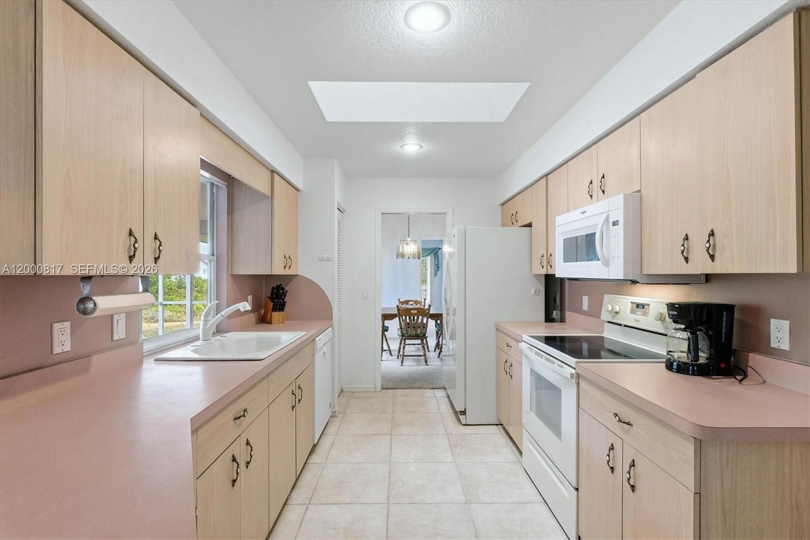 A galley-style kitchen features light wood cabinets, pink laminate countertops, and white appliances — PORT CHARLOTTE, FL