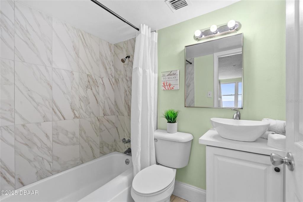 A bathroom features a marble-tiled shower, a white vanity with a vessel sink, and light-green walls — 2301 S ATLANTIC AVENUE UNIT 501, DAYTONA BEACH, FL