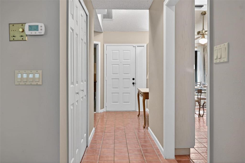A hallway with terracotta tile flooring leads to a white front door and entryway — 603 WATERWOOD DRIVE, YALAHA, FL