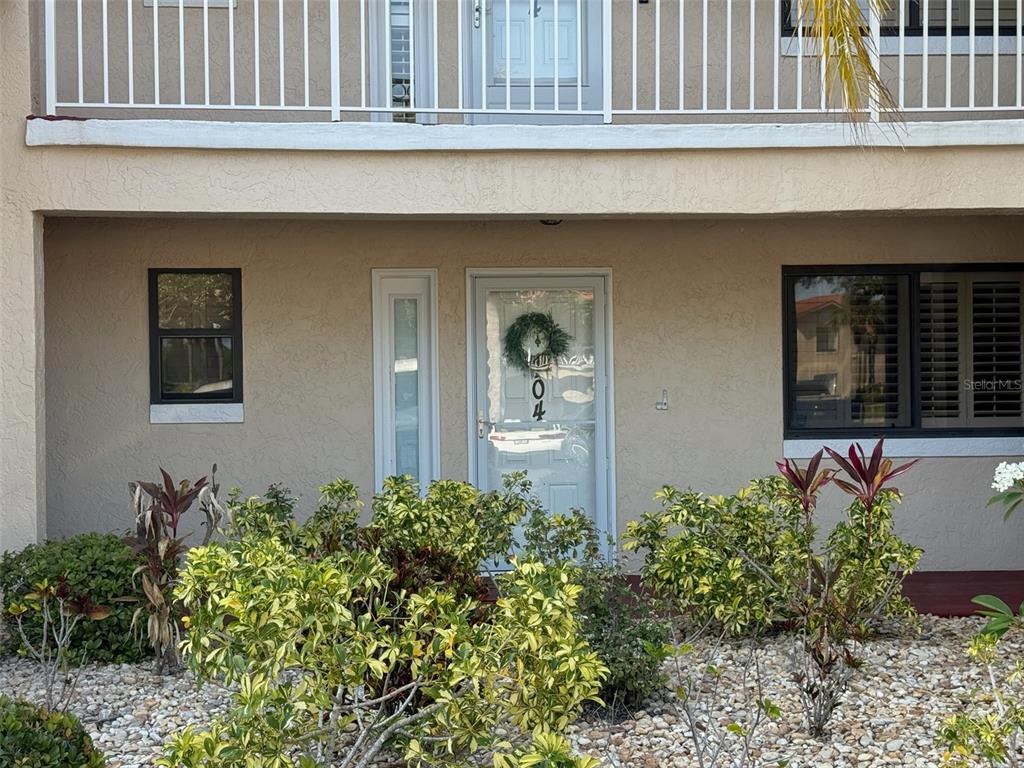 The exterior of a ground-floor unit features a white storm door, windows, and landscaping — 460 BOUCHELLE DRIVE UNIT 104, NEW SMYRNA BEACH, FL