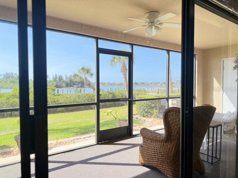 A screened-in porch features a ceiling fan, wicker furniture, and a view of the water — 460 BOUCHELLE DRIVE UNIT 104, NEW SMYRNA BEACH, FL