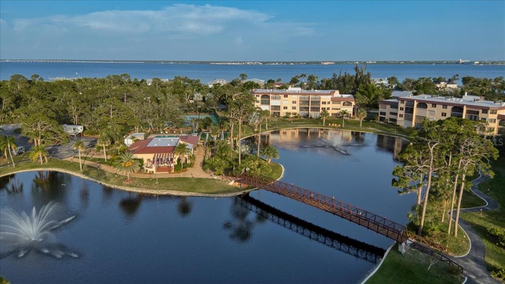 An aerial view of a pond with a fountain, a footbridge, and surrounding apartment buildings — 23465 HARBORVIEW ROAD UNIT 824, PUNTA GORDA, FL