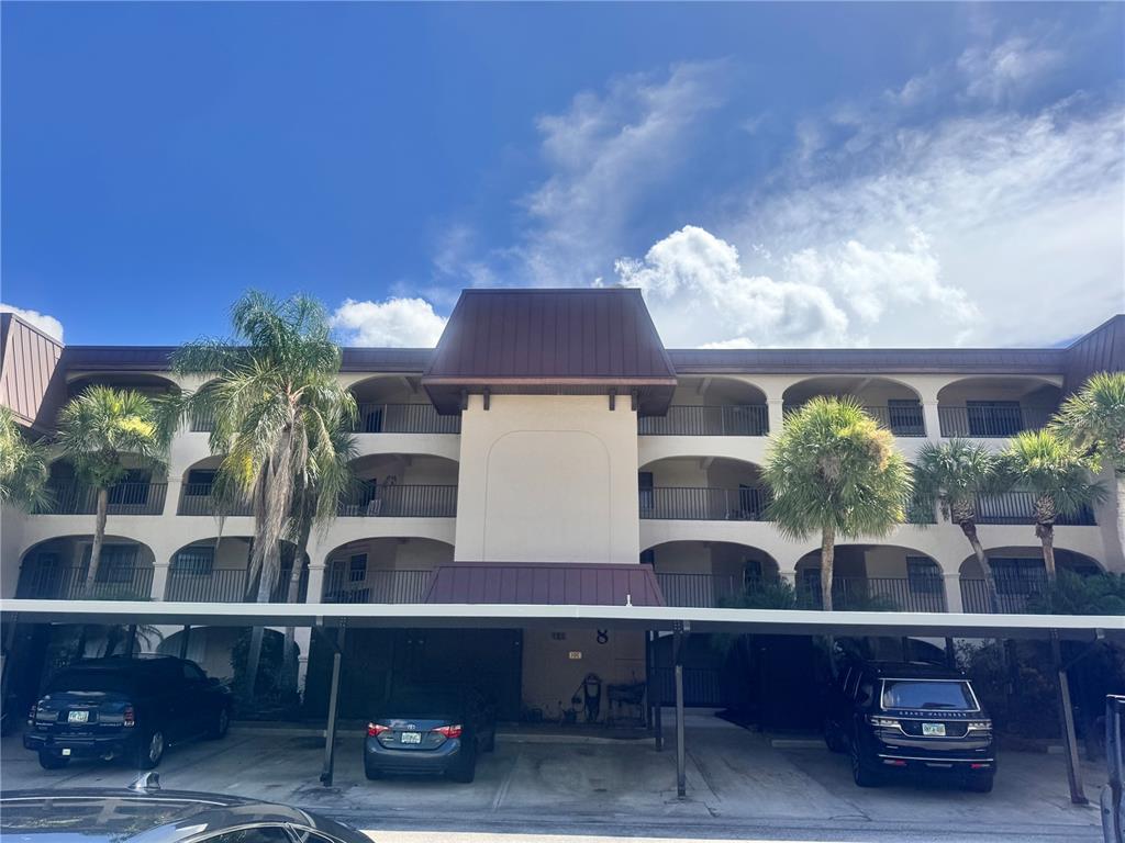 A three-story apartment building with a covered parking area and palm trees in front — 23465 HARBORVIEW ROAD UNIT 824, PUNTA GORDA, FL