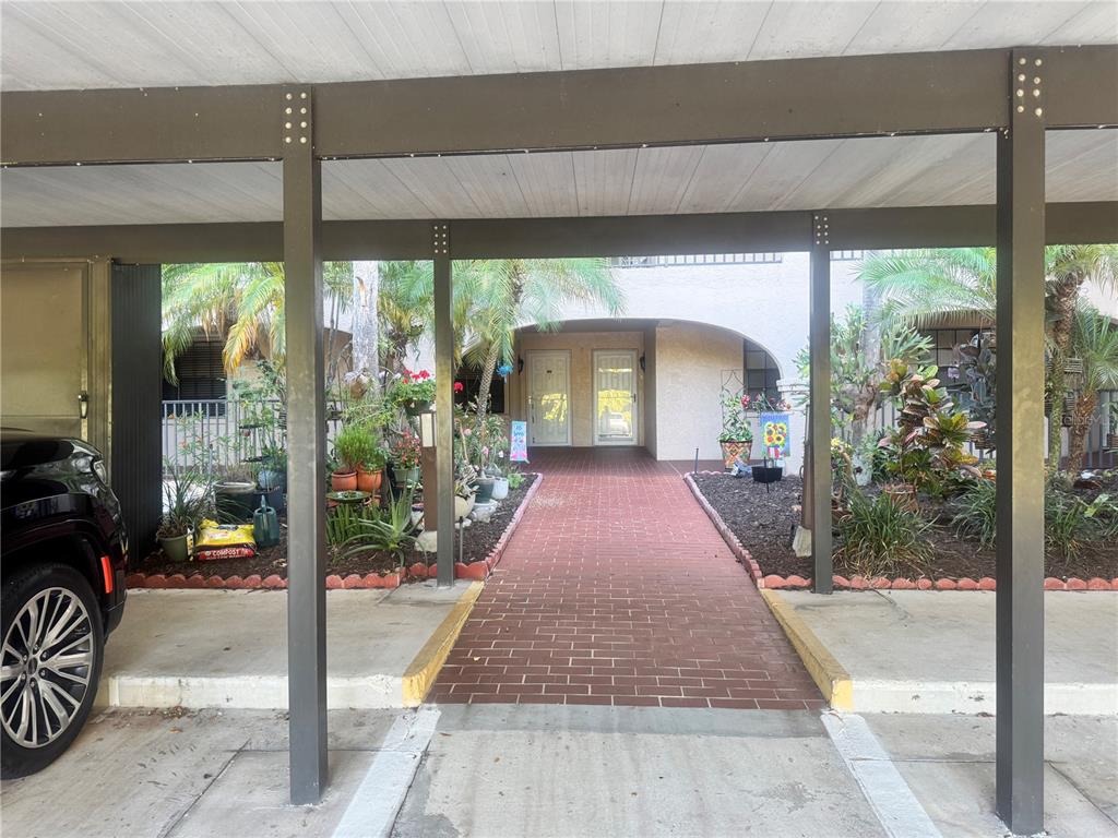 A brick walkway leads to two front doors under a covered carport with metal supports — 23465 HARBORVIEW ROAD UNIT 824, PUNTA GORDA, FL