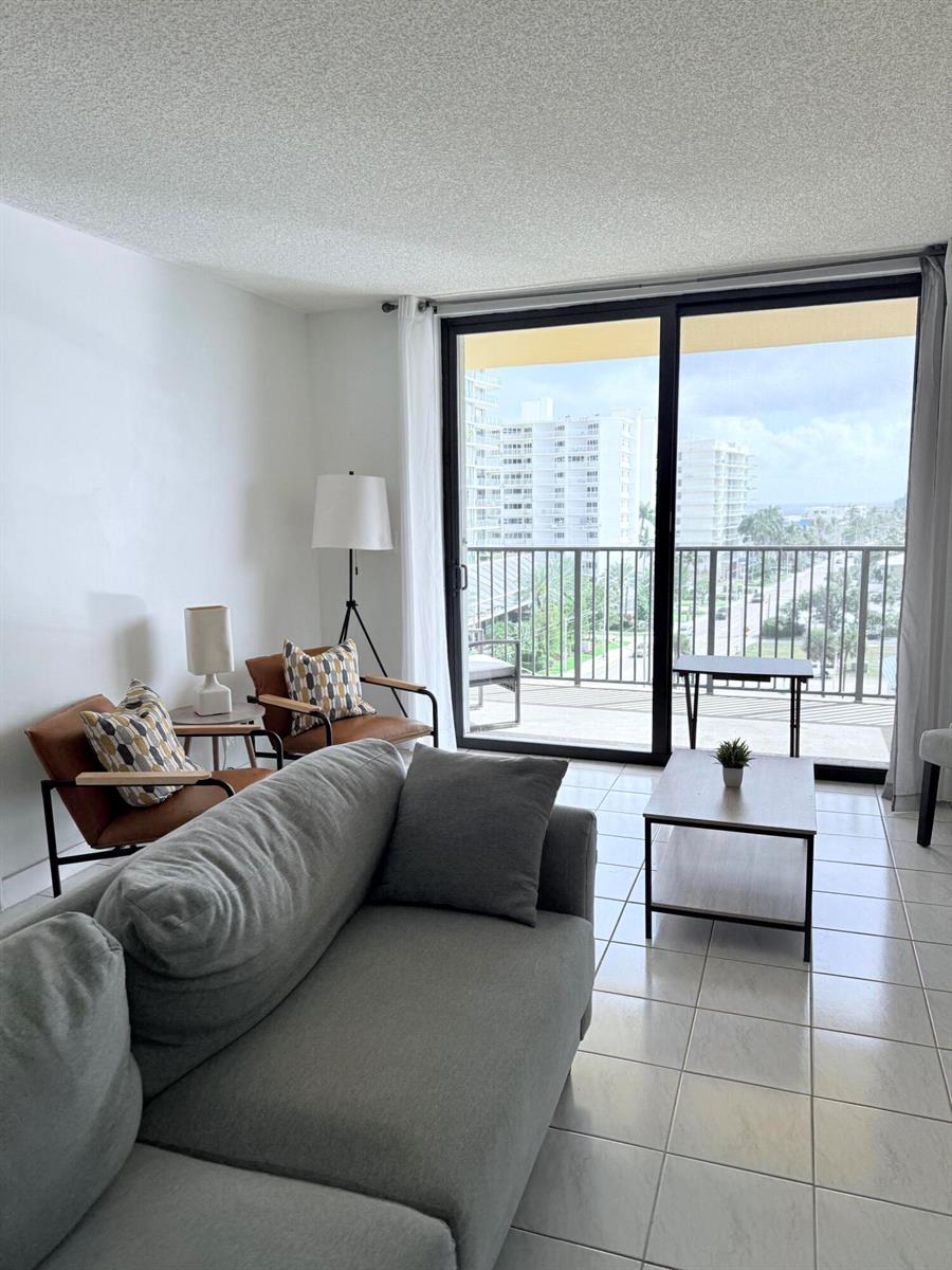 A living room features a grey sofa, two leather armchairs, and a balcony with city views — 801 N Ocean Boulevard # 802, Pompano Beach FL 33062, POMPANO BEACH, FL