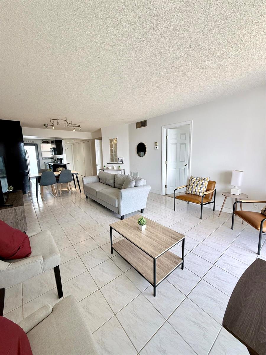 A living room with light tile flooring, a gray sofa, and two leather accent chairs — 801 N Ocean Boulevard # 802, Pompano Beach FL 33062, POMPANO BEACH, FL