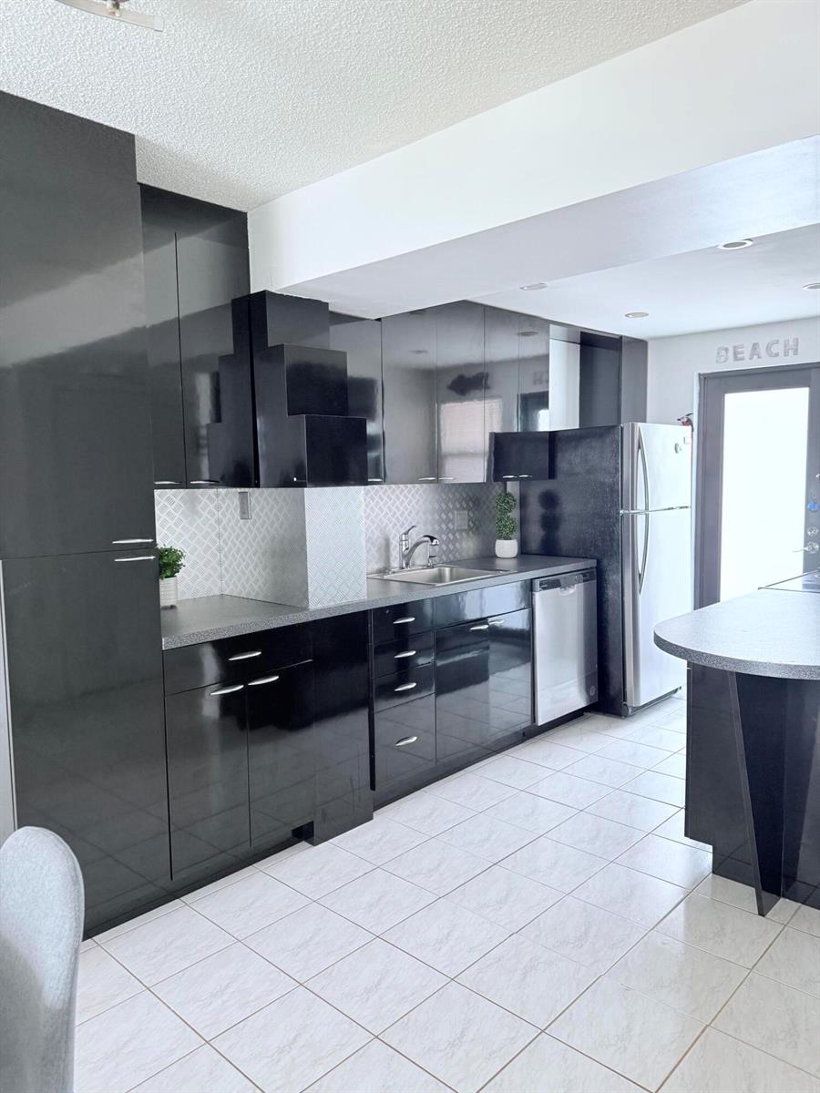 A kitchen features glossy black cabinets, a silver backsplash, and white tiled flooring — 801 N Ocean Boulevard # 802, Pompano Beach FL 33062, POMPANO BEACH, FL