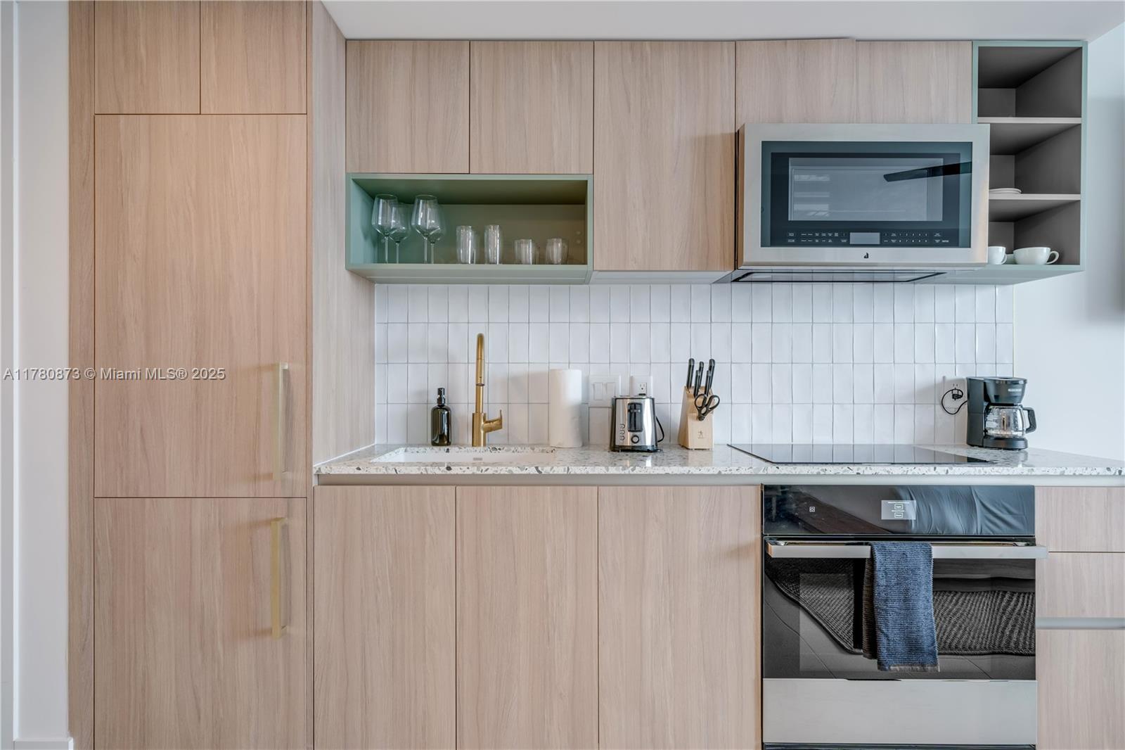 A modern kitchen features light wood cabinets, a white tiled backsplash, and a built-in microwave — 601 NE 1st Ave # 4212, Miami FL 33132, MIAMI, FL