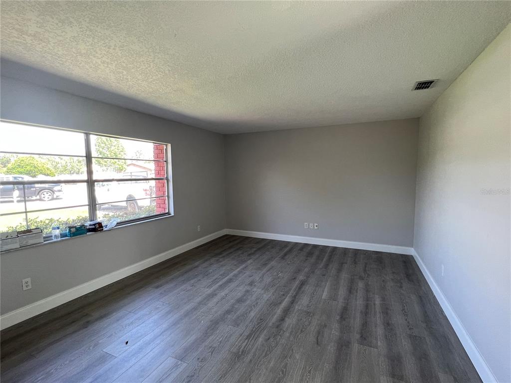 An empty room features gray walls, dark wood-look flooring, and a large window — 1313 SUMMER BREEZE ROAD, ORLANDO, FL