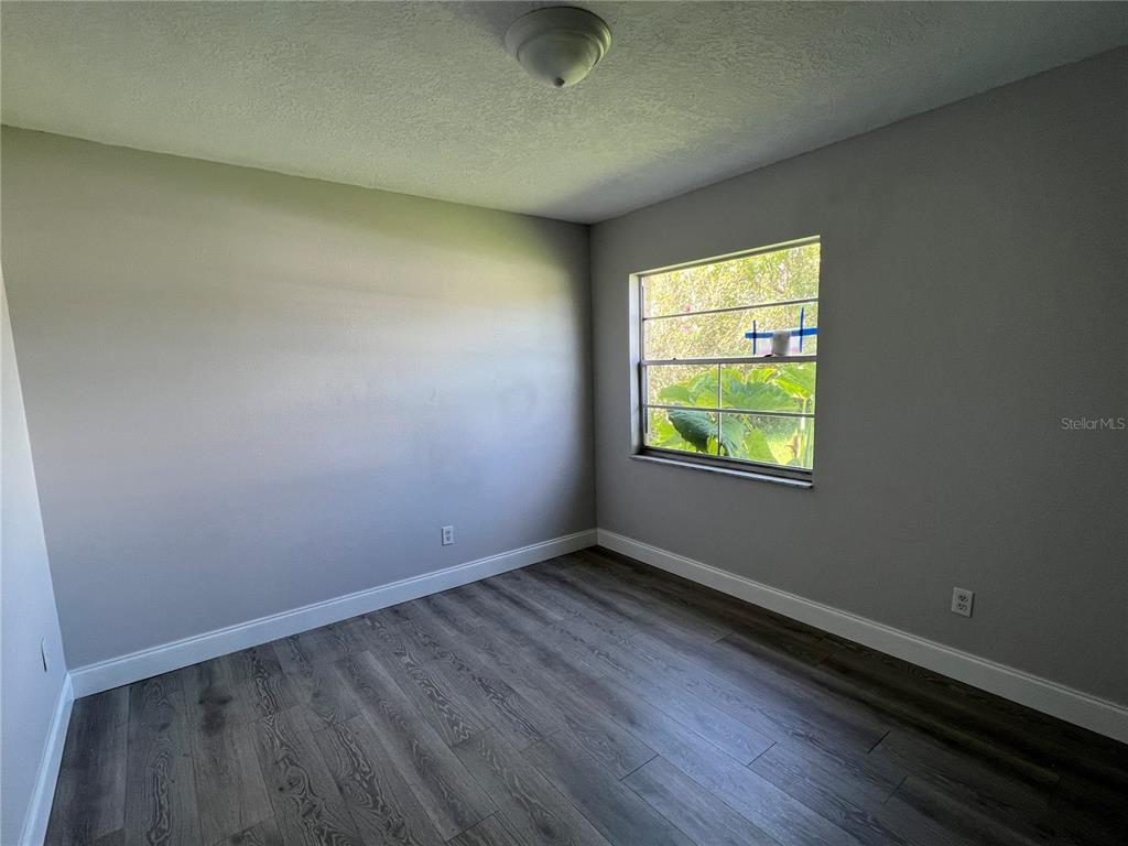 An empty bedroom features gray walls, wood-look flooring, and a window overlooking green foliage — 1313 SUMMER BREEZE ROAD, ORLANDO, FL