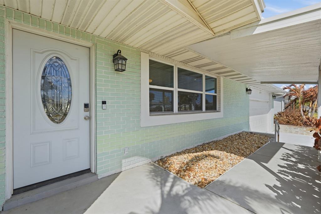 The exterior of a house features a light green brick wall, a white door, and a carport — 341 PLAZA BOULEVARD, DAYTONA BEACH, FL