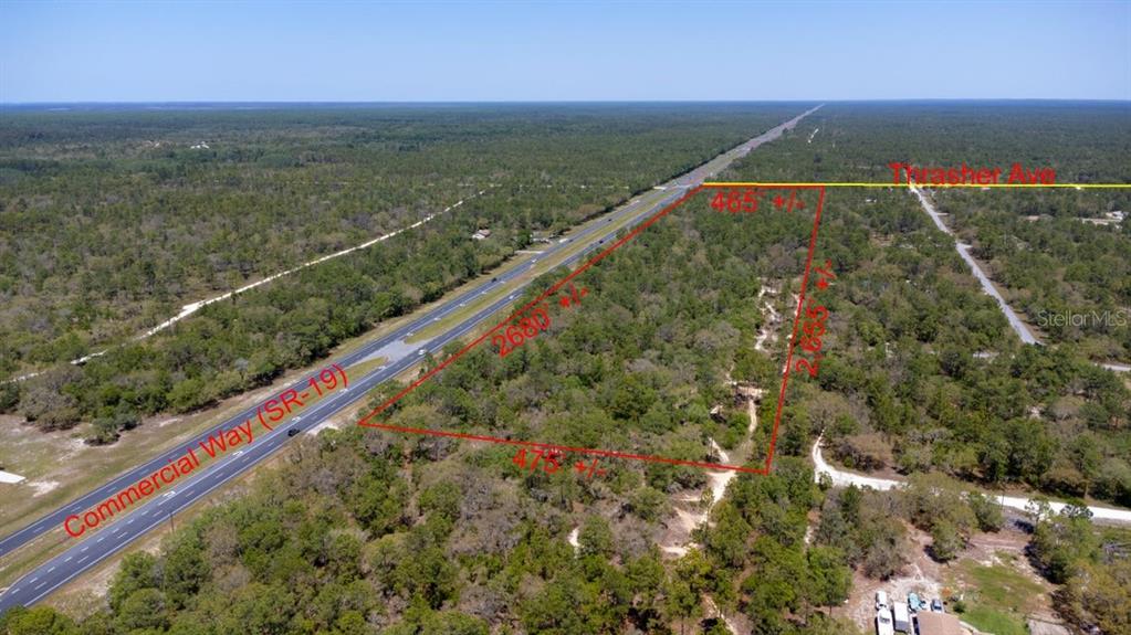 An aerial view shows a large, undeveloped plot of land bordering a highway — 0 THRASHER AVE, WEEKI WACHEE, FL
