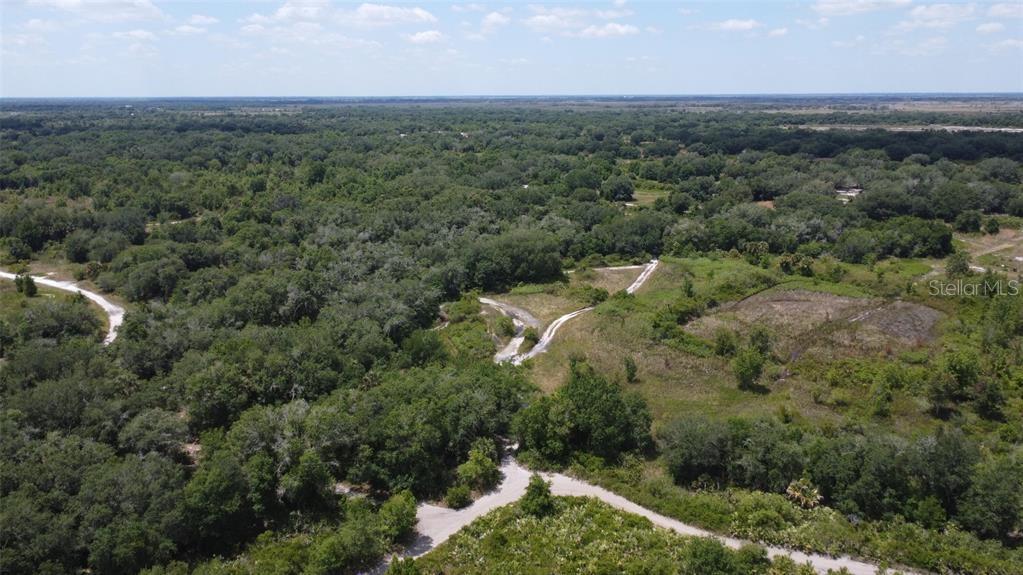 An aerial view shows a dirt path winding through a dense, wooded landscape — NW 300TH STREET, OKEECHOBEE, FL