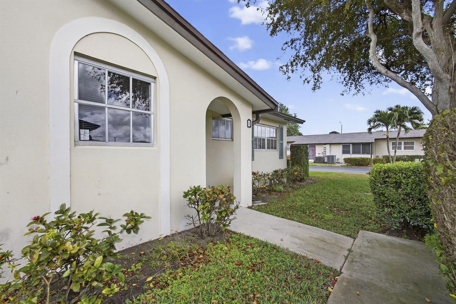 A beige exterior wall features an arched entryway and a window with white trim — 2960 Ashley Drive E # D, West Palm Beach FL 33415, WEST PALM BEACH, FL