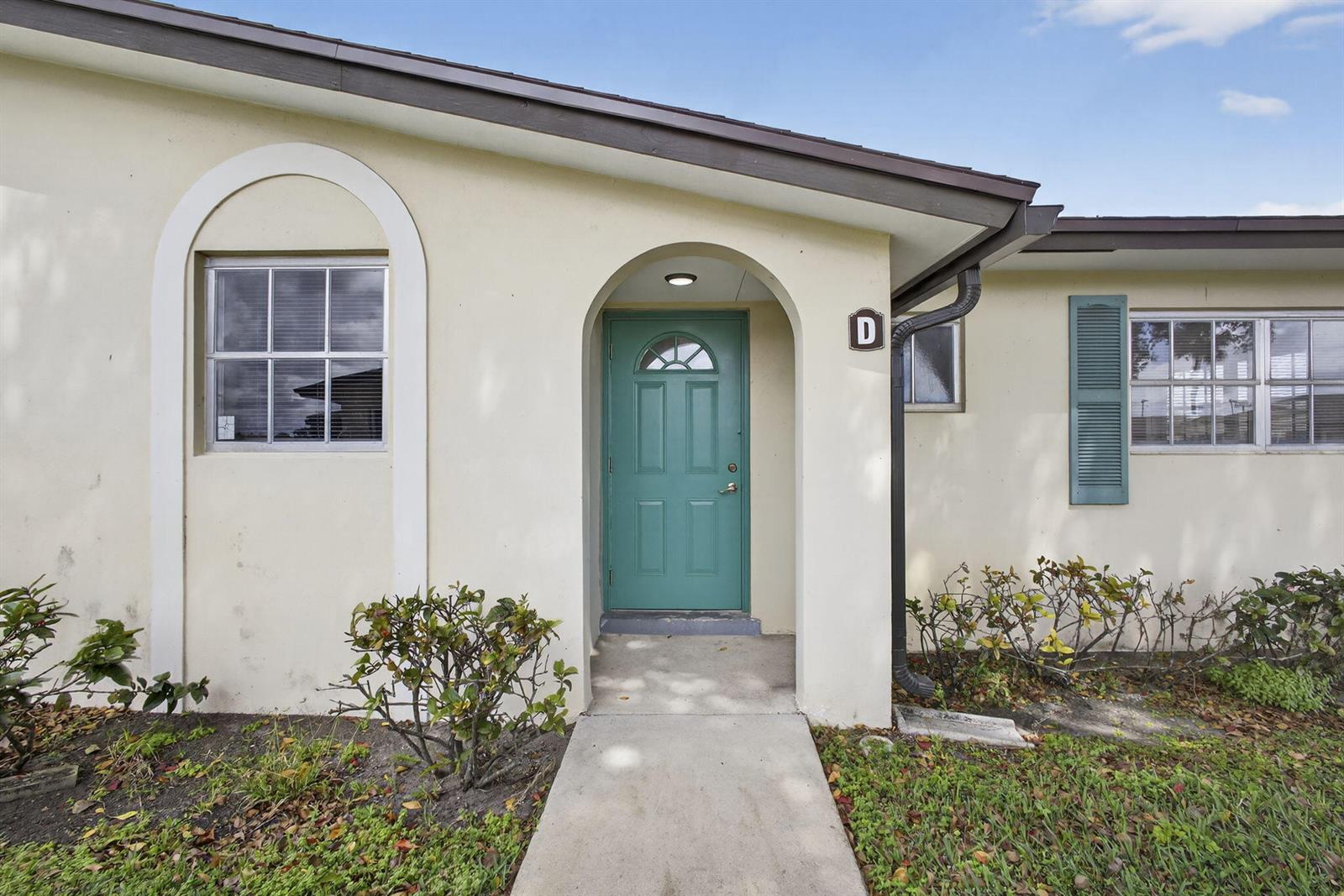 The exterior of a single-story unit features a teal front door and a concrete walkway — 2960 Ashley Drive E # D, West Palm Beach FL 33415, WEST PALM BEACH, FL