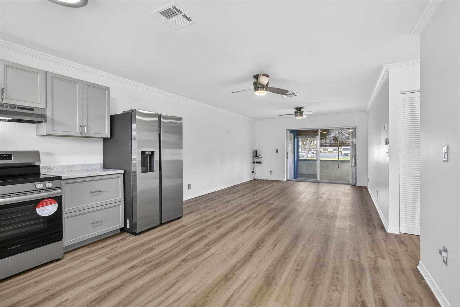 A kitchen with grey cabinets and stainless steel appliances opens into a living area — 2960 Ashley Drive E # D, West Palm Beach FL 33415, WEST PALM BEACH, FL