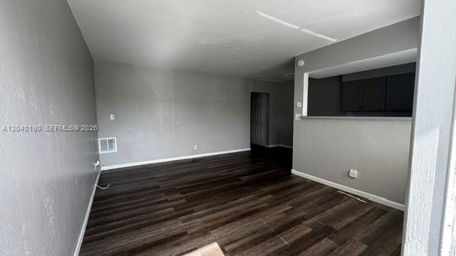 An empty living room with dark wood-look flooring, grey walls, and a kitchen pass-through window — FORT LAUDERDALE, FL