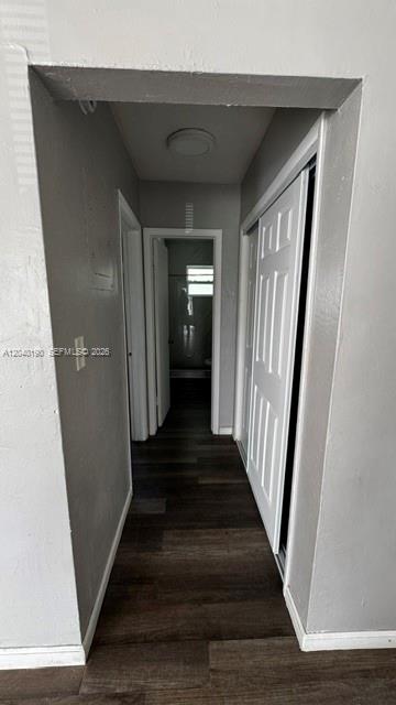 A hallway with dark wood-look flooring leads to a bathroom with a white door — FORT LAUDERDALE, FL