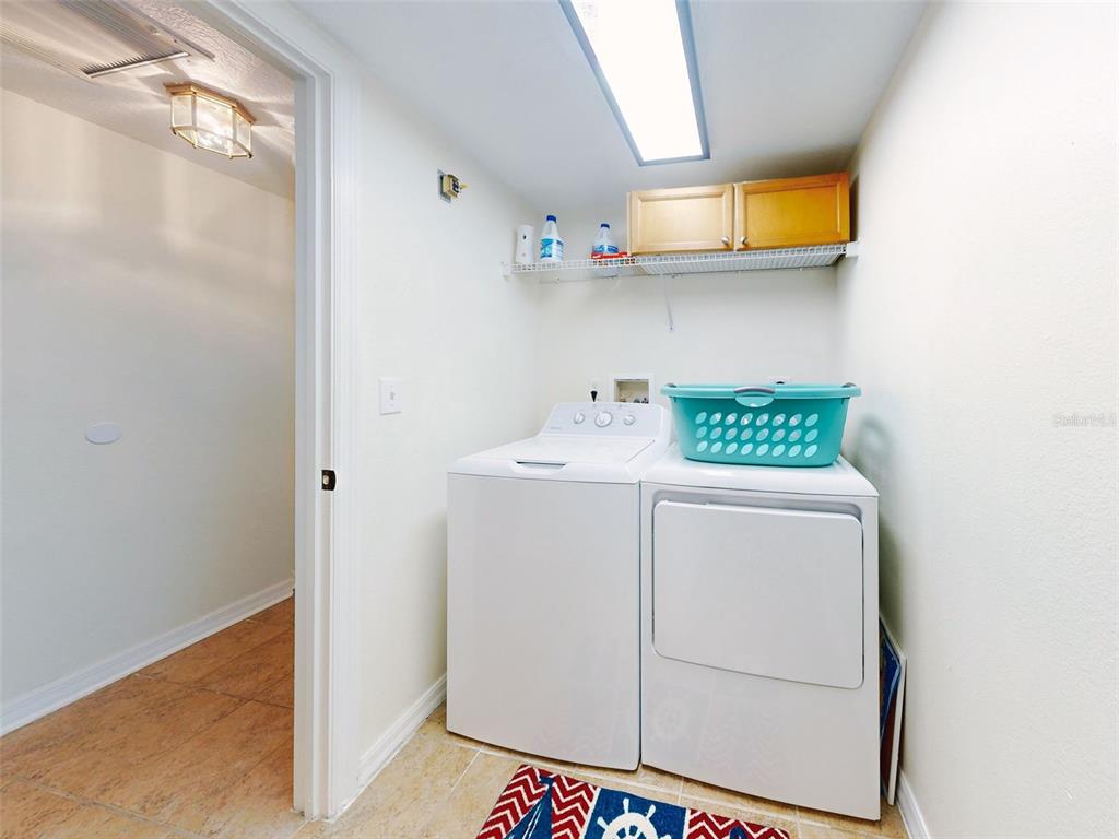 A laundry room features a white washer and dryer, wire shelving, and a wooden cabinet — 5300 S ATLANTIC AVENUE UNIT 1-203, NEW SMYRNA BEACH, FL