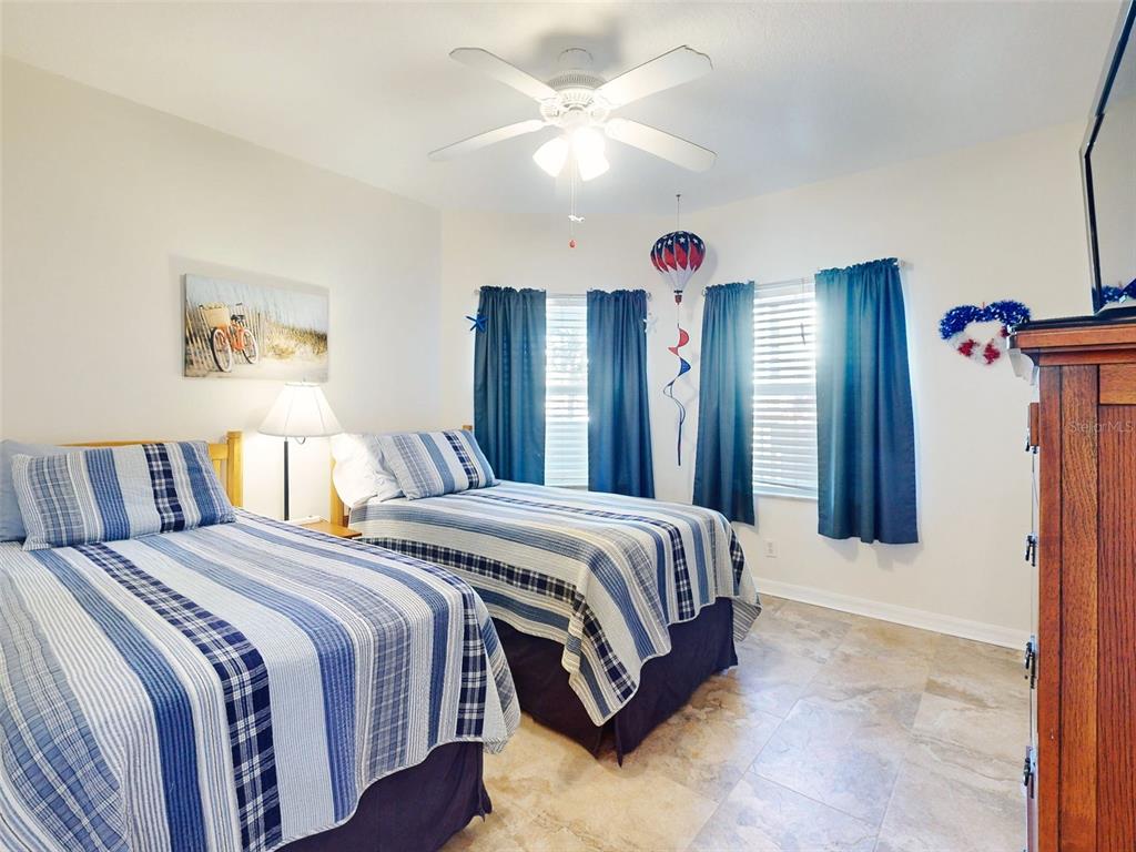 A bedroom features two twin beds with blue striped bedding, tile flooring, and blue curtains — 5300 S ATLANTIC AVENUE UNIT 1-203, NEW SMYRNA BEACH, FL