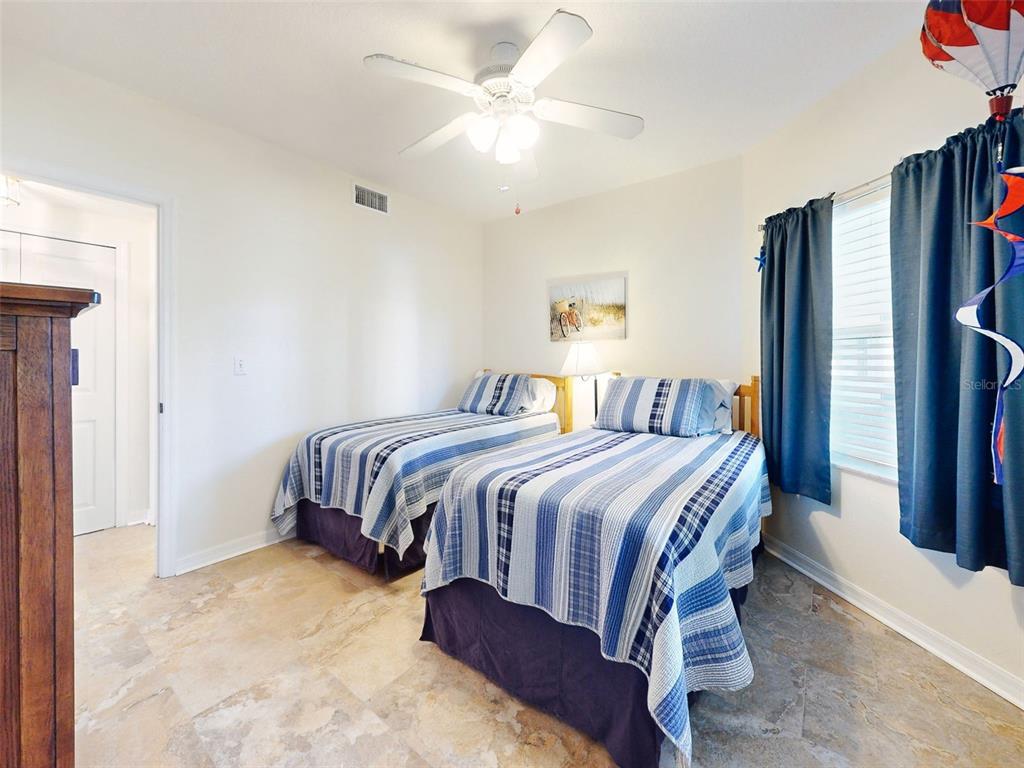 A bedroom features two twin beds with blue striped bedding, tile flooring, and a ceiling fan — 5300 S ATLANTIC AVENUE UNIT 1-203, NEW SMYRNA BEACH, FL