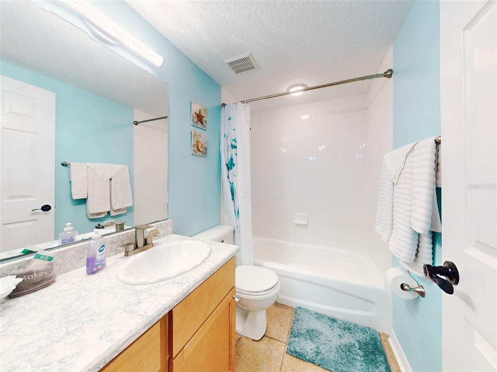 A bathroom features light blue walls, a wood vanity with a stone countertop, and a tub — 5300 S ATLANTIC AVENUE UNIT 1-203, NEW SMYRNA BEACH, FL