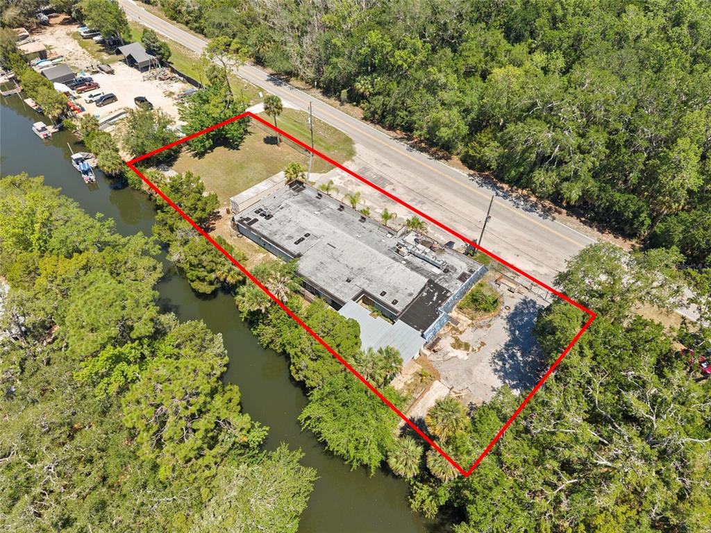 An aerial view shows a rectangular commercial building situated between a road and a canal — 6018 & 6024 CORTEZ BOULEVARD, WEEKI WACHEE, FL