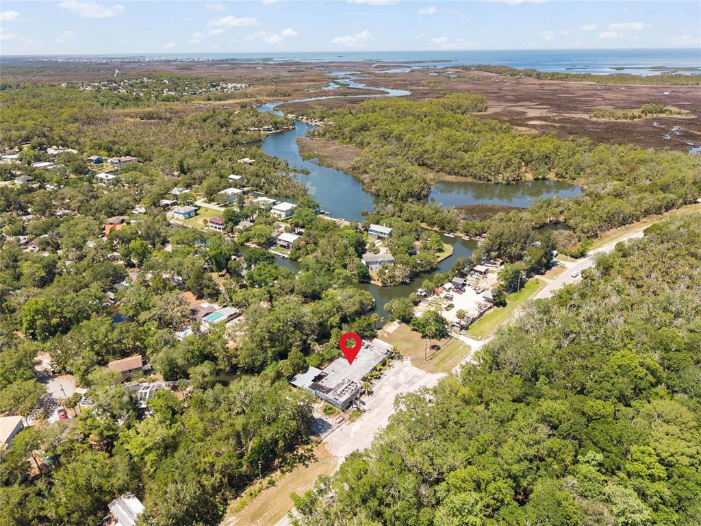 An aerial view shows a commercial building with a parking lot surrounded by dense trees — 6018 & 6024 CORTEZ BOULEVARD, WEEKI WACHEE, FL