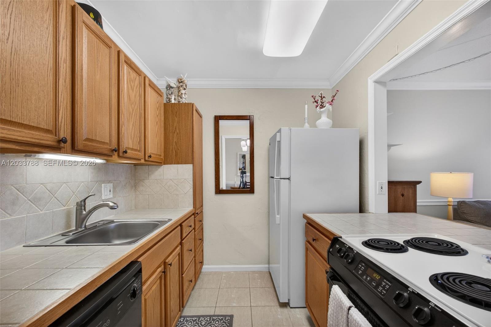 A kitchen features oak cabinets, tiled countertops, a white refrigerator, and a black stove — 112 Doolen Ct # 306, North Palm Beach FL 33408, NORTH PALM BEACH, FL