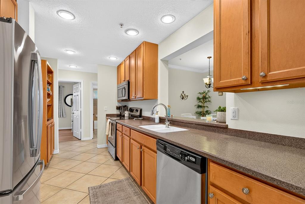 A kitchen with wood cabinets, stainless steel appliances, and a pass-through window to the dining area — 7228 HAMILTON ROAD UNIT 7228, BRADENTON, FL