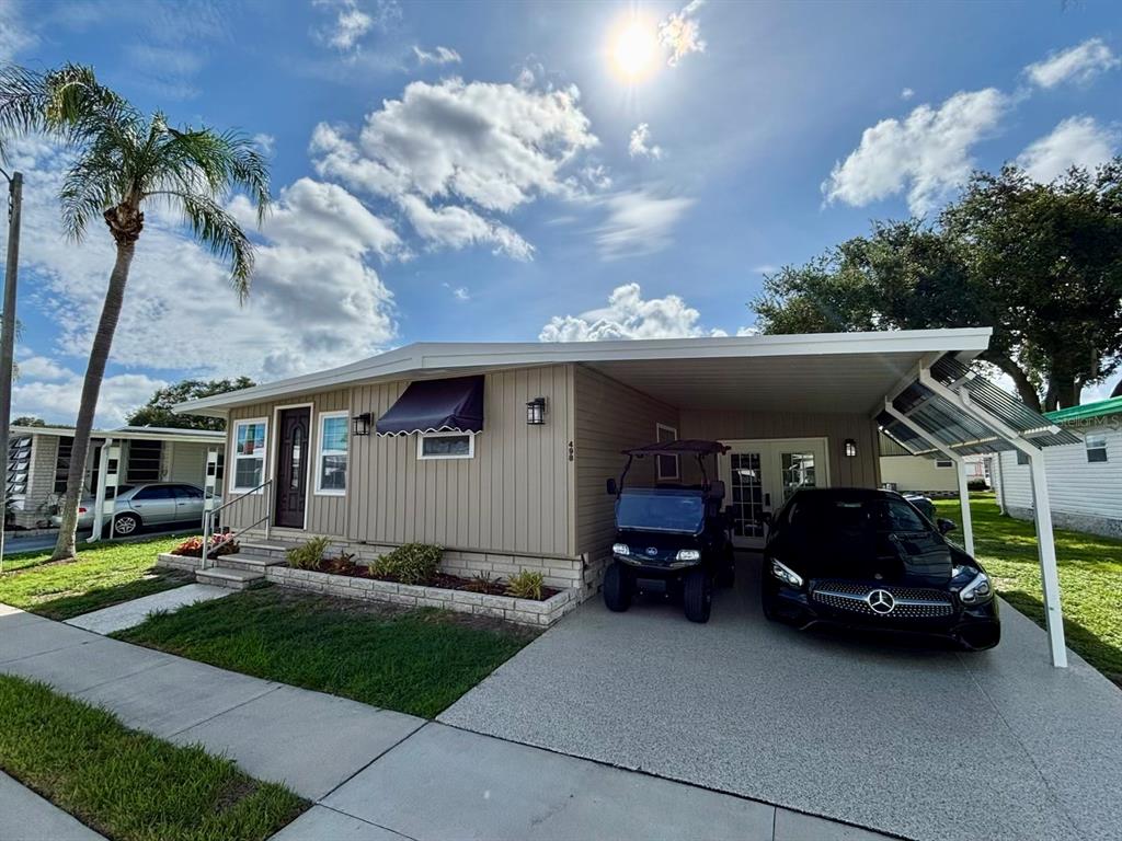 A single-story manufactured home with a carport, a golf cart, and a black car — 1100 BELCHER ROAD S UNIT 498, LARGO, FL