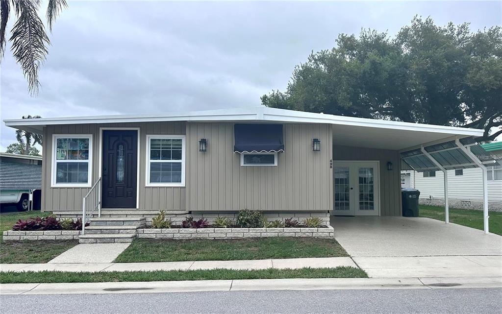 A single-story manufactured home with tan vertical siding, a front porch, and an attached carport — 1100 BELCHER ROAD S UNIT 498, LARGO, FL