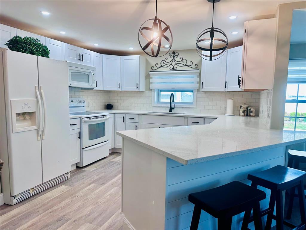 A kitchen features white cabinetry, quartz countertops, a subway tile backsplash, and two pendant lights — 1100 BELCHER ROAD S UNIT 498, LARGO, FL