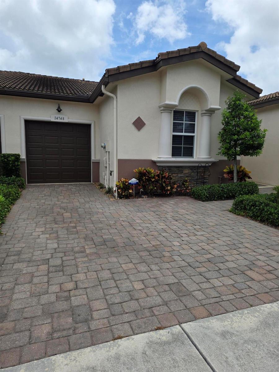 The exterior of a beige stucco house features palm trees, stone accents, and landscaped gardens — 14748 Barletta Way, Delray Beach FL 33446, DELRAY BEACH, FL