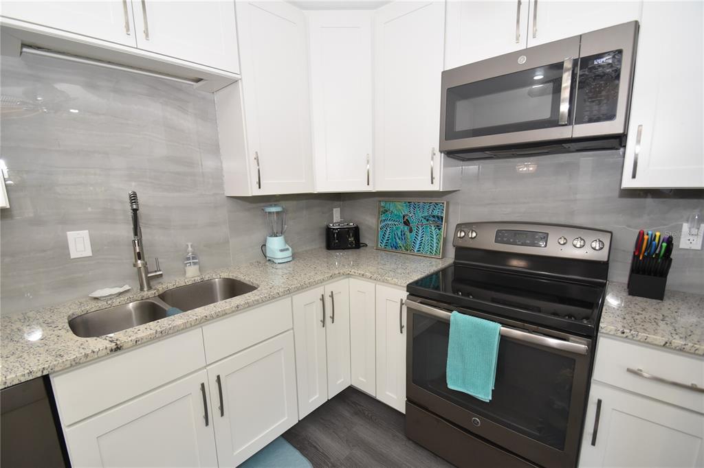 A kitchen features white cabinets, granite countertops, stainless steel appliances, and a gray tile backsplash — 1647 BROOKHOUSE COURT UNIT BR146, SARASOTA, FL