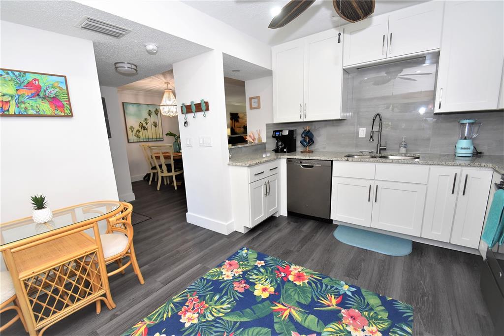 A kitchen with white cabinets, stainless steel appliances, and a tropical-themed rug on gray flooring — 1647 BROOKHOUSE COURT UNIT BR146, SARASOTA, FL