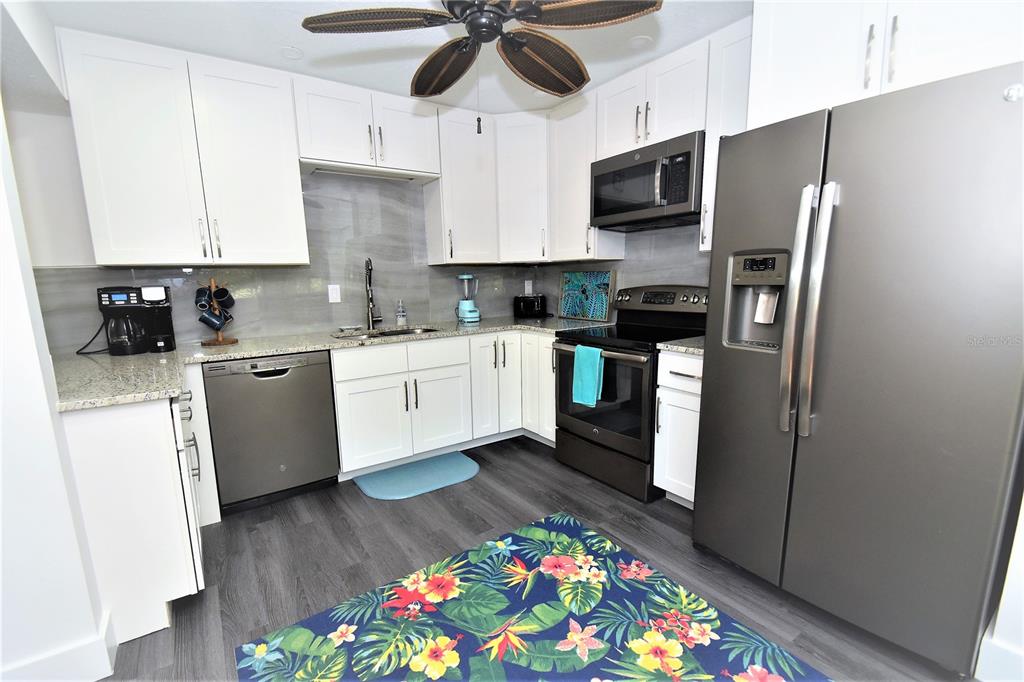 A kitchen features white cabinets, stainless steel appliances, a gray backsplash, and a floral rug — 1647 BROOKHOUSE COURT UNIT BR146, SARASOTA, FL