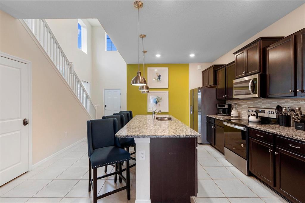 A kitchen features dark wood cabinets, granite countertops, a central island, and a yellow accent wall — 3413 LILAC, DAVENPORT, FL
